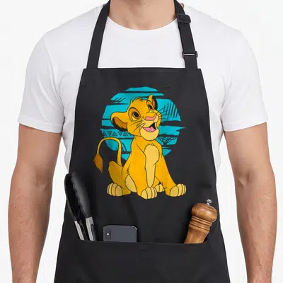 Tablier de cuisine noir avec une illustration colorée d'un jeune lion assis et souriant sur fond bleu.