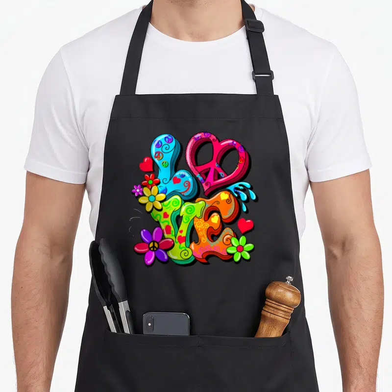 Tablier de cuisine noir avec Peace Love en lettres colorées, fleurs hippies et symboles de paix rétro.