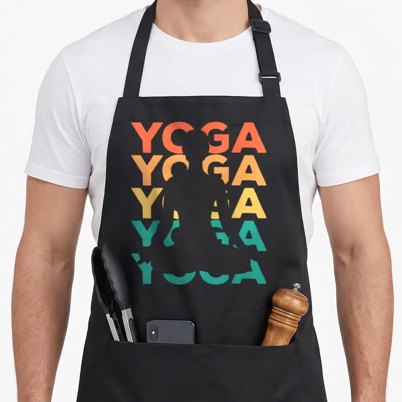 Tablier de cuisine noir avec le mot YOGA répété en dégradé coloré et une silhouette de personne en posture de yoga au centre.