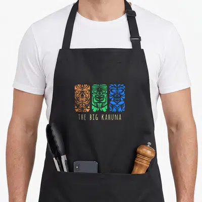 Tablier de cuisine noir avec trois masques tiki colorés et l'inscription The Big Kahuna en bas.