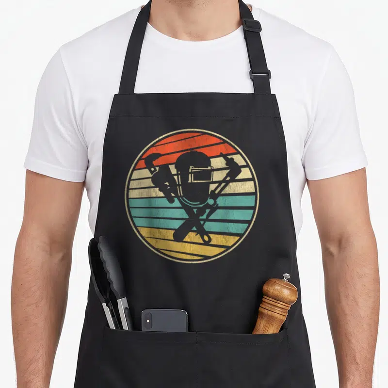 Tablier de cuisine noir avec illustration circulaire rétro montrant un casque de soudier et des outils croisés.