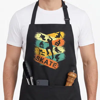 Tablier de cuisine noir avec illustration rétro de skateboarders et le mot SKATE sur bandes colorées.