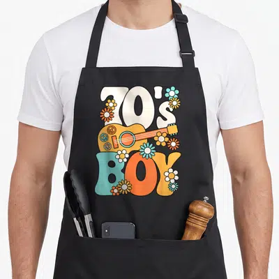 Tablier de cuisine noir avec illustration 70's Boy, guitare orange, symboles de la paix et fleurs multicolores dans un style rétro.