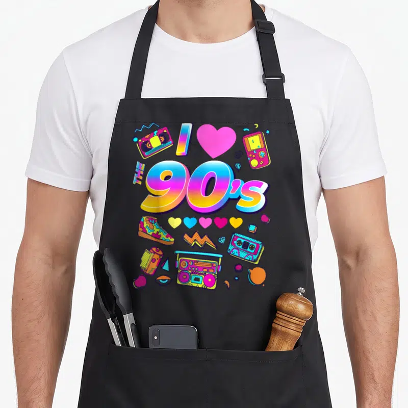 Tablier de cuisine noir avec le texte The 90's et des illustrations rétro comme une boombox, une cassette et des cœurs colorés.
