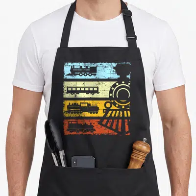Tablier de cuisine noir avec motifs de trains vintage sur bandes bleue, jaune, orange et rouge ainsi que des engrenages mécaniques.