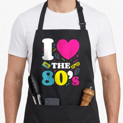Tablier de cuisine noir avec le texte I love the 80's entouré d'un cœur rose et d'icônes rétro colorées.