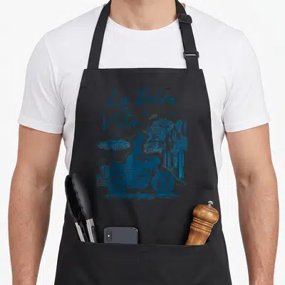 Tablier de cuisine noir avec une illustration bleue d'une femme en moto devant les bâtiments de Positano et le texte La Dolce Vita.