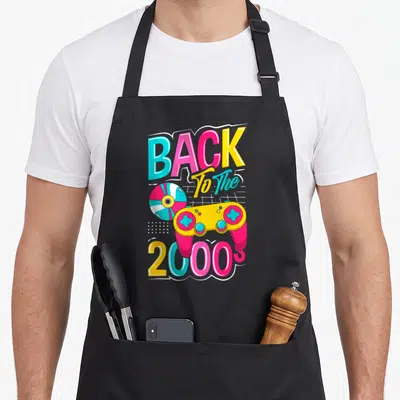Tablier de cuisine noir avec illustration colorée d'une manette jaune et rose et un disque compact sur fond graphique.