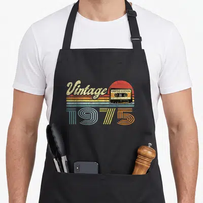 Tablier de cuisine noir avec illustration de cassette audio rétro, le mot Vintage et l'année 1975 en lettres colorées.
