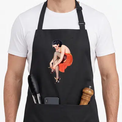 Tablier de cuisine noir avec illustration d'une femme en robe orange ajustant ses chaussures à talons hauts noirs et nœuds jaunes.
