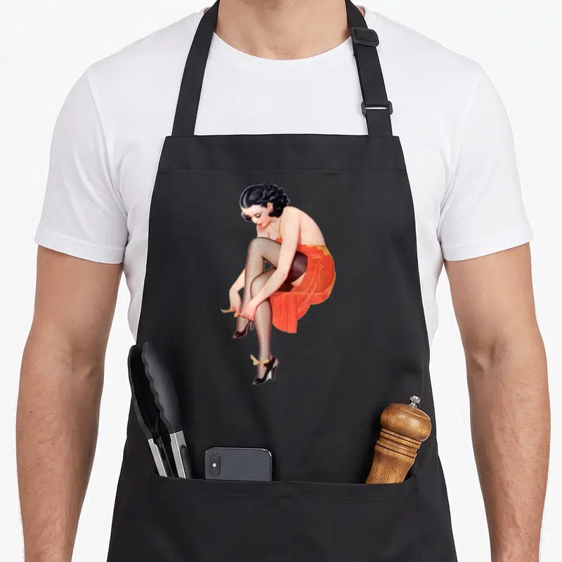 Tablier de cuisine noir avec illustration d'une femme en robe orange ajustant ses chaussures à talons hauts noirs et nœuds jaunes.