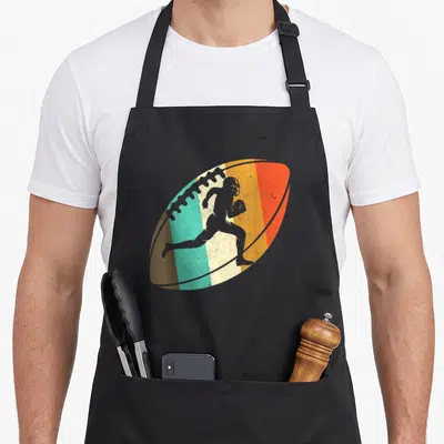 Tablier de cuisine noir avec illustration d'un ballon de football américain aux couleurs rétro et silhouette de joueur courant.