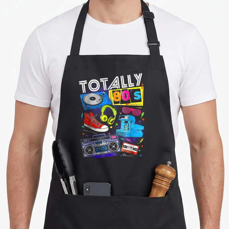 Tablier de cuisine noir avec illustration coloréeTotally 80s, boombox, platine vinyle et sneakers rouges.