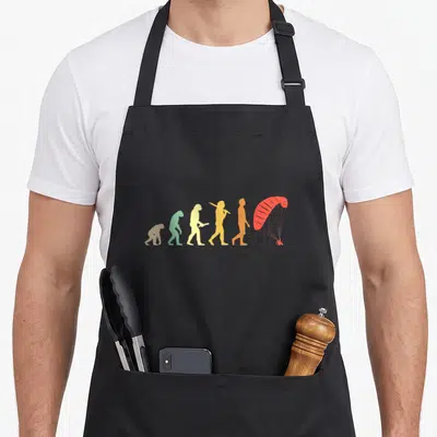 Tablier de cuisine noir avec illustration colorée de l'évolution humaine se terminant par un parapente rouge.