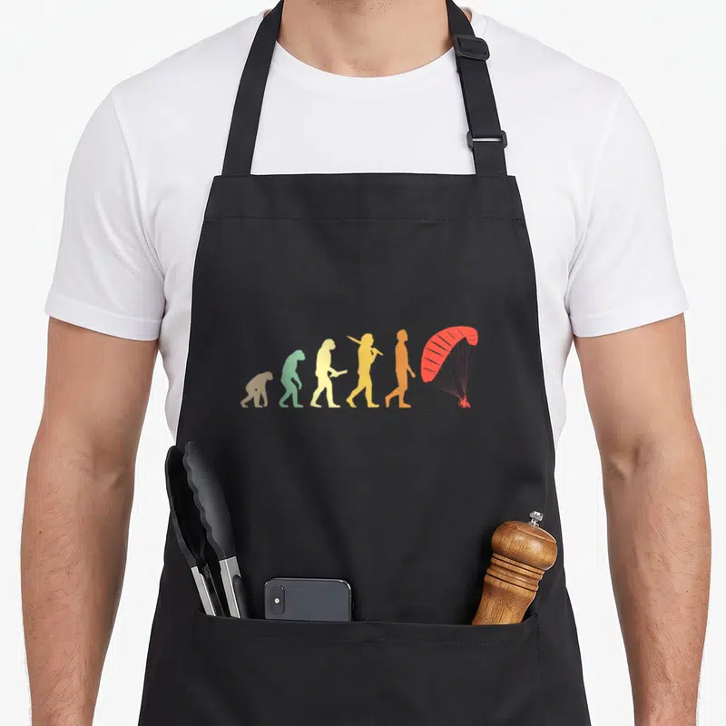 Tablier de cuisine noir avec illustration colorée de l'évolution humaine se terminant par un parapente rouge.