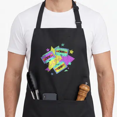 Tablier de cuisine noir avec trois cassettes magnétophones colorées, étoiles et triangles géométriques sur fond texturé.