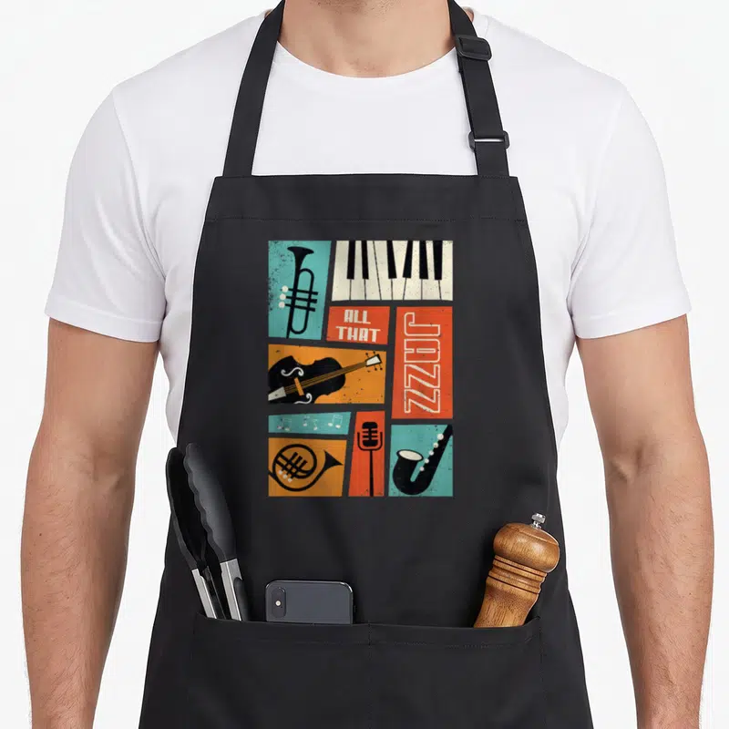 Tablier de cuisine noir avec illustration retro jazz montrant piano, trompette, violoncelle et micro sur fond coloré géométrique.