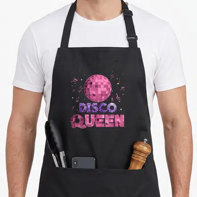 Tablier de cuisine noir avec une boule disco rose et l'inscription Disco Queen en lettres miroir.