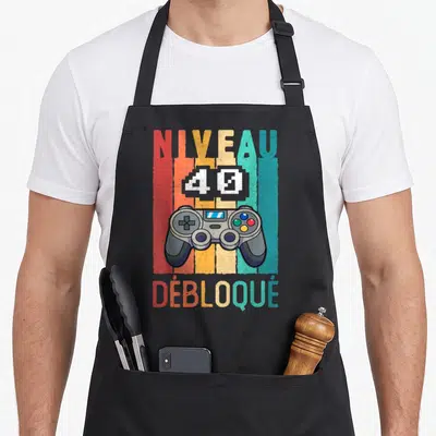 Tablier de cuisine noir avec une manette de jeu vidéo et le texte Niveau 40 Débloqué en style rétro coloré.