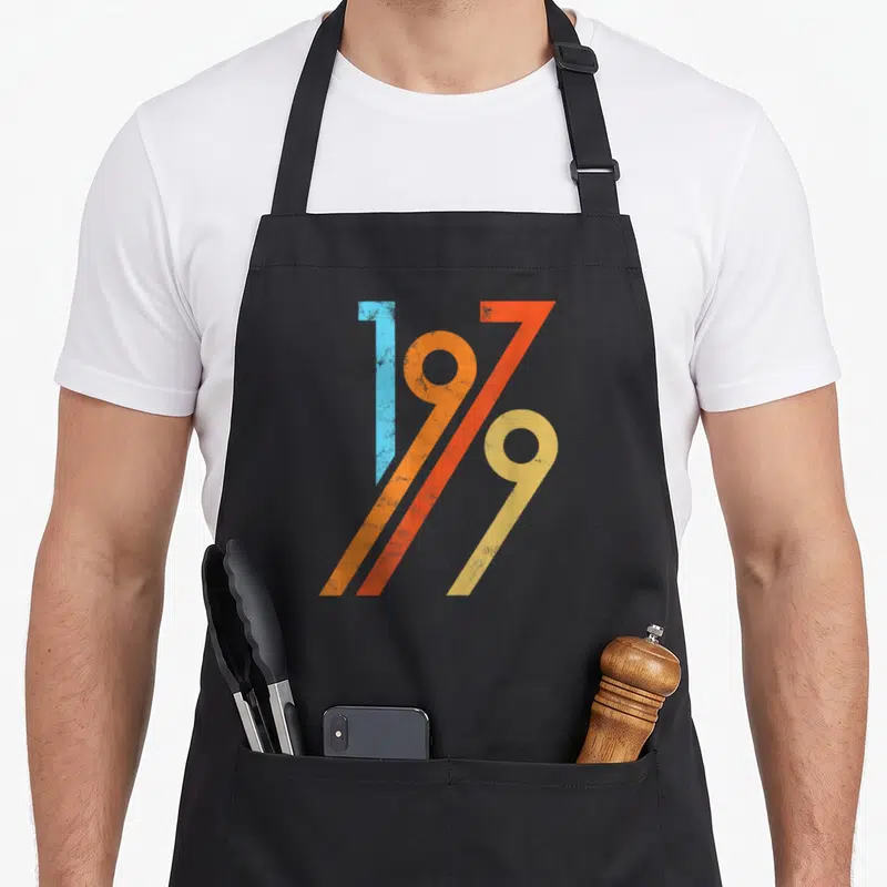 Tablier de cuisine noir avec le motif graphique 1979 aux couleurs vives et effet vieilli.