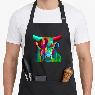 Tablier de cuisine noir avec une illustration de tête de vache aux multiples couleurs et formes géométriques anguleuses.
