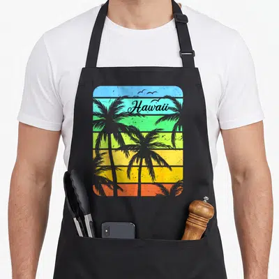 Tablier de cuisine noir avec illustration rétro Hawaii palmiers et texte Aloha sur fond rayé coloré.