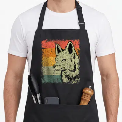 Tablier de cuisine noir avec illustration d'un renard rétro sur fond de bandes colorées délavées orange et vert.