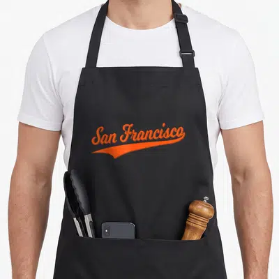 Tablier de cuisine noir avec l'inscription San Francisco en écriture cursive orange et un trait dynamique sous le texte.