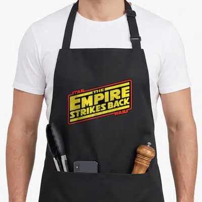 Tablier de cuisine noir avec le logo rectangulaire The Empire Strikes Back Star Wars en jaune et rouge sur fond sombre.