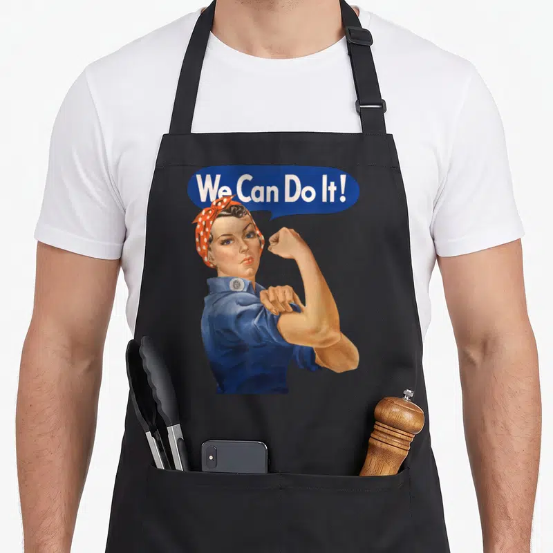 Tablier de cuisine noir avec illustration de Rosie The Riveter et bulle We Can Do It en bleu et blanc.