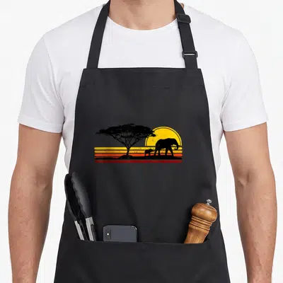 Tablier de cuisine noir avec silhouette d'éléphant, acacia et coucher de soleil rétro aux bandes horizontales orange et jaune.