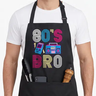 Tablier de cuisine noir avec l'inscription 80s Bro, une radio cassette et une console de jeu colorée sur fond gris uni.