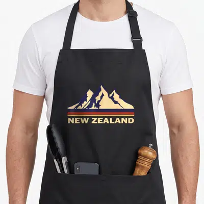 Tablier de cuisine noir avec illustration de montagnes New Zealand style rétro et bandes colorées.