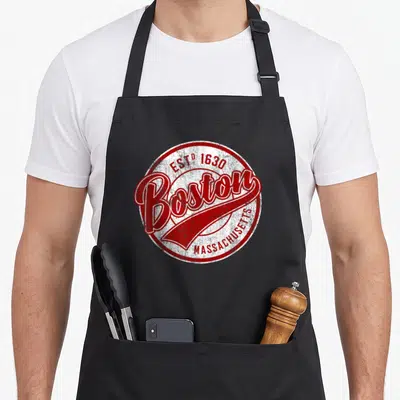 Tablier de cuisine noir avec un logo rond rouge et blanc portant le nom Boston Massachusetts et la date Est 1630.