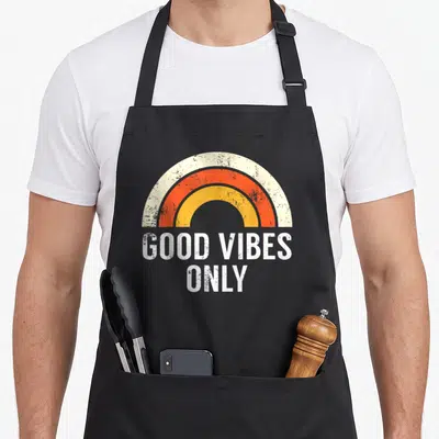 Tablier de cuisine noir avec arc en ciel orange jaune et texte « Good Only » en blanc délavé.