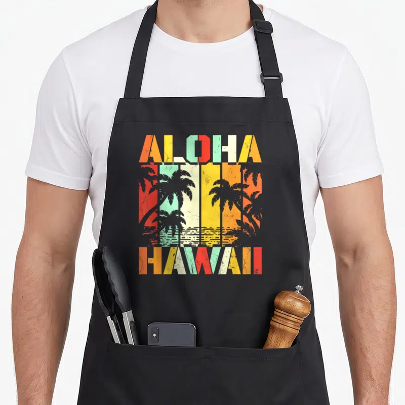 Tablier de cuisine noir avec inscription Aloha Hawaii et silhouettes de palmiers multicolores sur fond rayé.