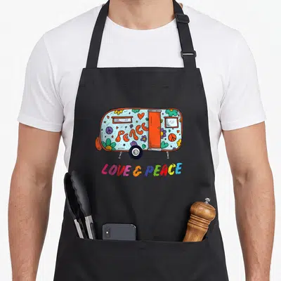 Tablier de cuisine noir avec une caravane colorée ornée de fleurs, de symboles de la paix et des mots Peace Love & Peace.
