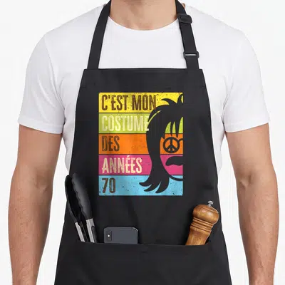 Tablier de cuisine noir avec l'inscription C'est mon costume des années 70 sur fond coloré et silhouette de coiffure rétro.