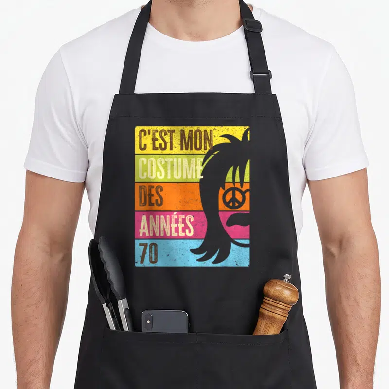 Tablier de cuisine noir avec l'inscription C'est mon costume des années 70 sur fond coloré et silhouette de coiffure rétro.