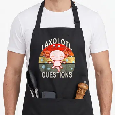 Tablier de cuisine noir avec illustration d'un axolotl rose souriant sur fond de soleil rétro aux bandes orange et vertes.