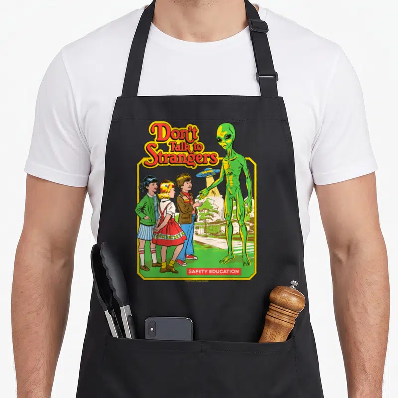 Tablier de cuisine noir avec une illustration retro montrant des enfants et un alien vert sous le texte Don't Talk to Strangers.