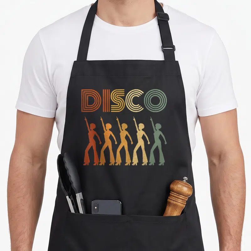 Tablier de cuisine noir avec l'inscription Disco et cinq silhouettes dansant en tenues évasées orange jaune et vert.
