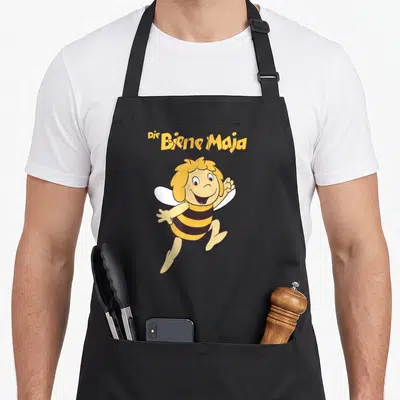 Tablier de cuisine noir avec l'abeille jaune rayée et le logo Die Biene Maja en lettres dorées au-dessus.