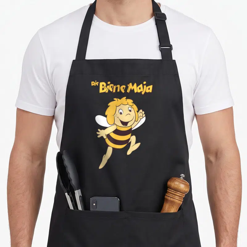 Tablier de cuisine noir avec l'abeille jaune rayée et le logo Die Biene Maja en lettres dorées au-dessus.
