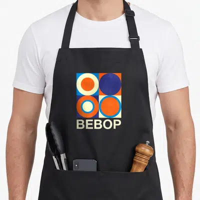 Tablier de cuisine noir avec motif géométrique rétro Bebop composé de cercles orange bleu et blanc sur fond quadrillé.