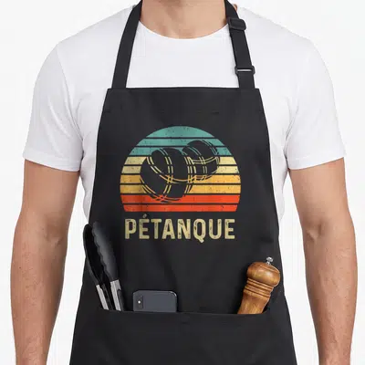 Tablier de cuisine noir avec illustration soleil rétro et trois boules de pétanque stylisées au centre.