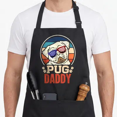 Tablier de cuisine noir avec un carlin portant des lunettes soleil aux couleurs du drapeau américain et le texte Pug Daddy.