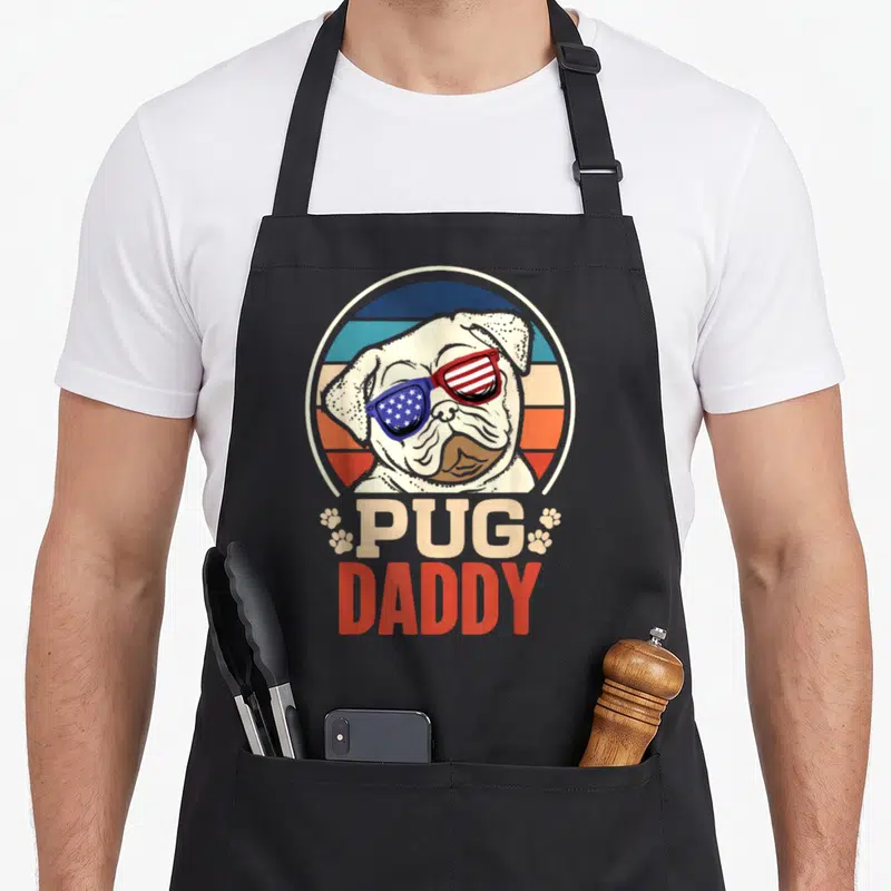 Tablier de cuisine noir avec un carlin portant des lunettes soleil aux couleurs du drapeau américain et le texte Pug Daddy.