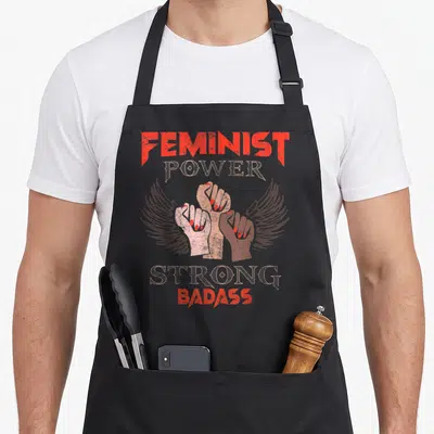 Tablier de cuisine noir avec trois poings levés aux ailes et texte Feminist Power Strong Badass en rouge et beige délavé.