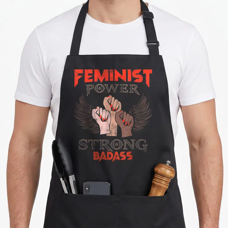Tablier de cuisine noir avec trois poings levés aux ailes et texte Feminist Power Strong Badass en rouge et beige délavé.